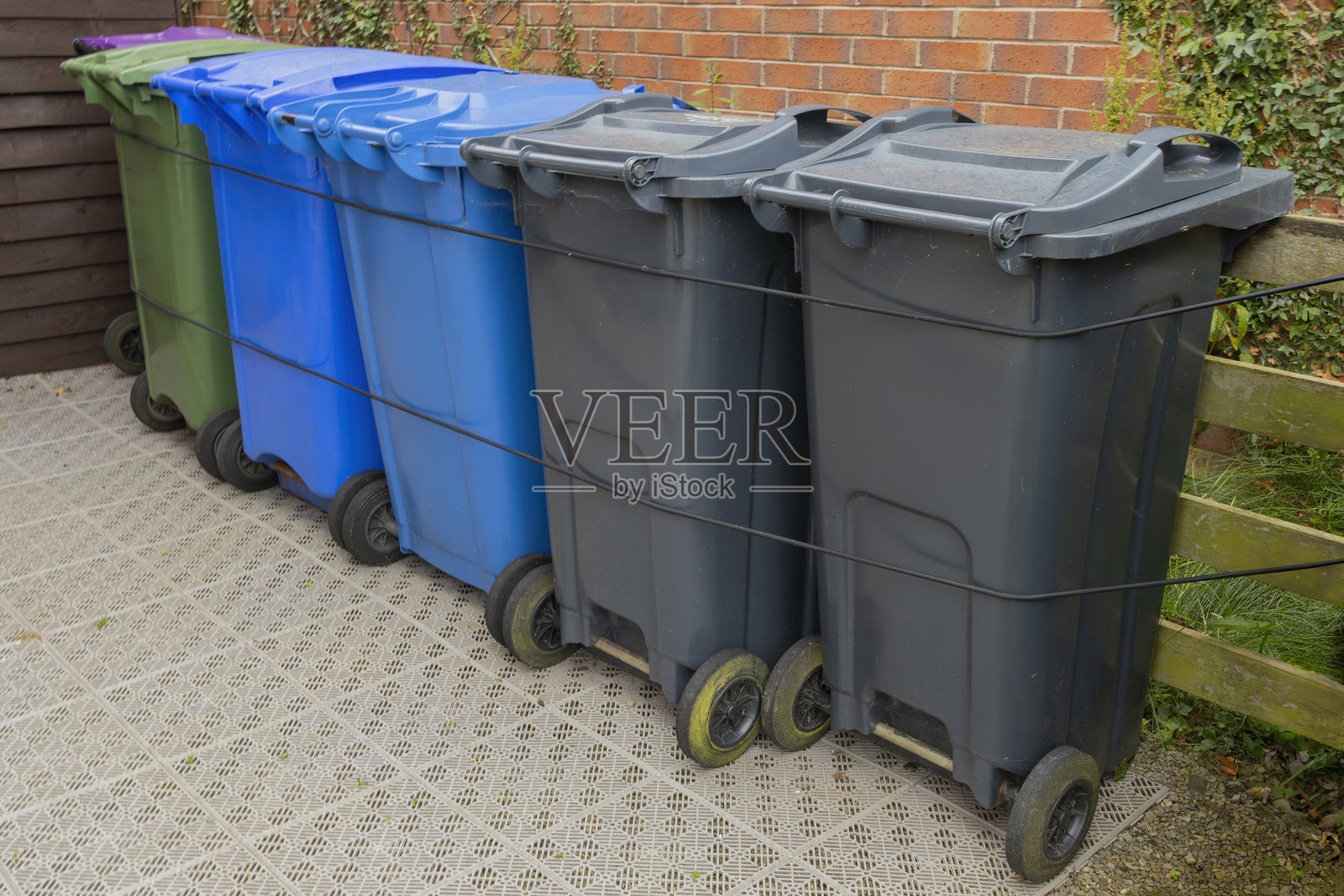 塑料废物回收垃圾桶整齐排列并固定在英国房屋砖墙旁的花园储藏区，等待每周的市政收集。照片摄影图片