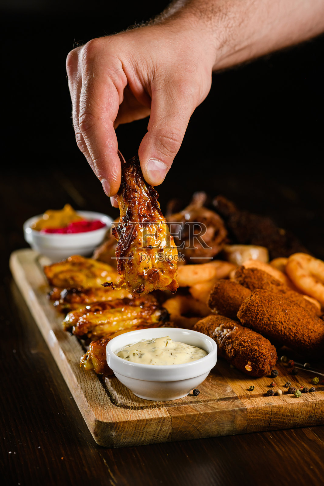 手握酥脆鸡翅，沾上酱汁照片摄影图片