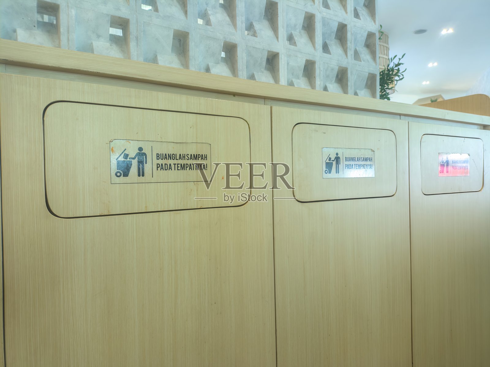 带有印尼语标志的木制垃圾桶，敦促正确的垃圾处理，位于现代、光线良好的公共空间。垃圾桶整齐排列，强调环保意识和卫生。照片摄影图片