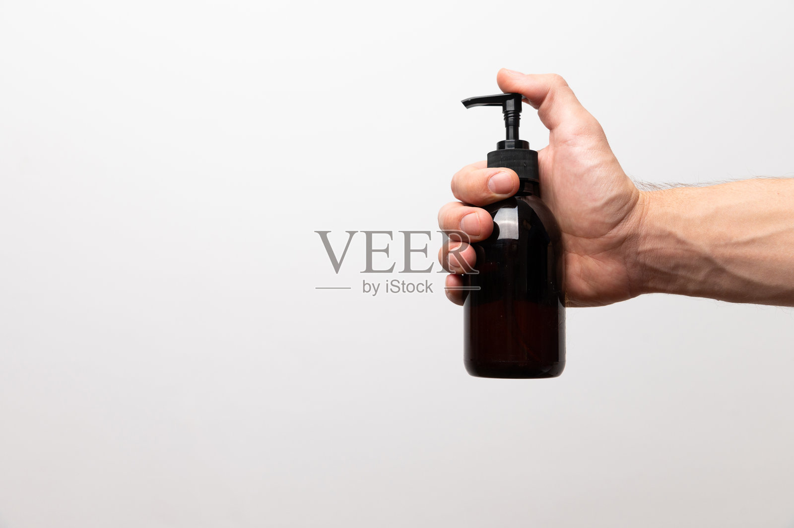 年轻男子手持大塑料瓶，瓶上有泵，背景为白色。关心身体肌肤的清洁与柔软。日常化妆品。特写镜头。照片摄影图片