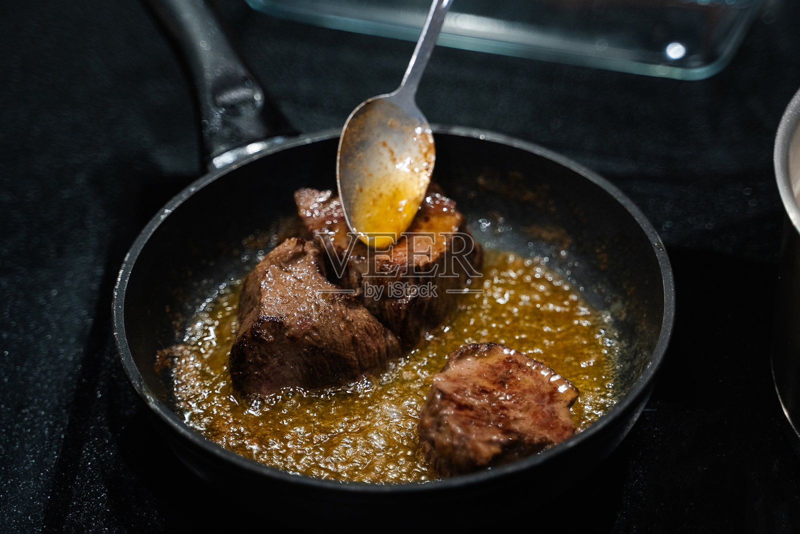 小块牛排在煎锅中煎炸，油被倒在肉上。照片摄影图片