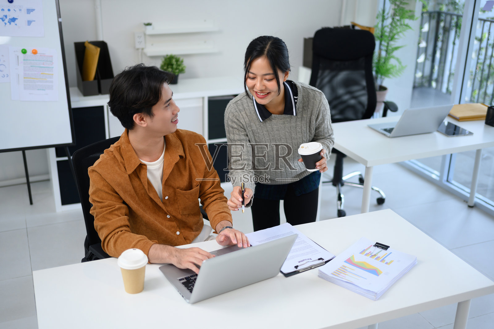 微笑的女性同事在办公室与同事通过笔记本电脑分享想法照片摄影图片