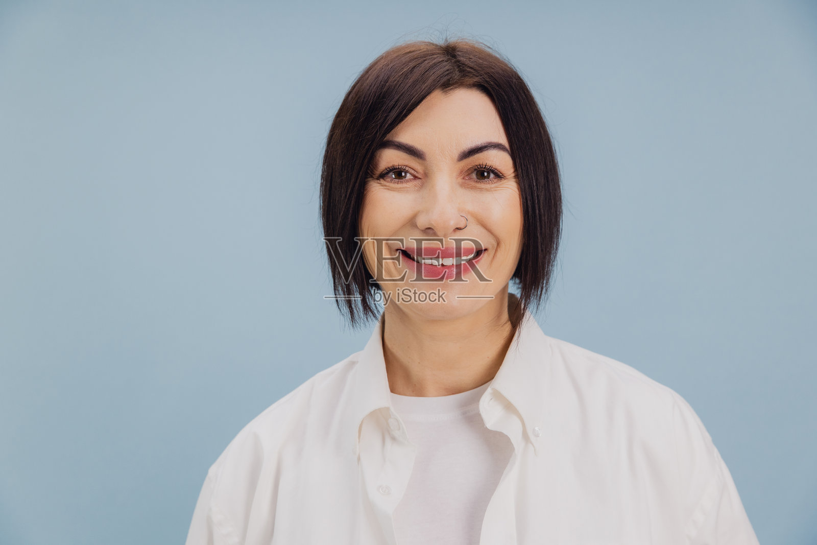 微笑的成熟的女性，鼻子上有穿孔，摆姿势于浅蓝色背景前照片摄影图片