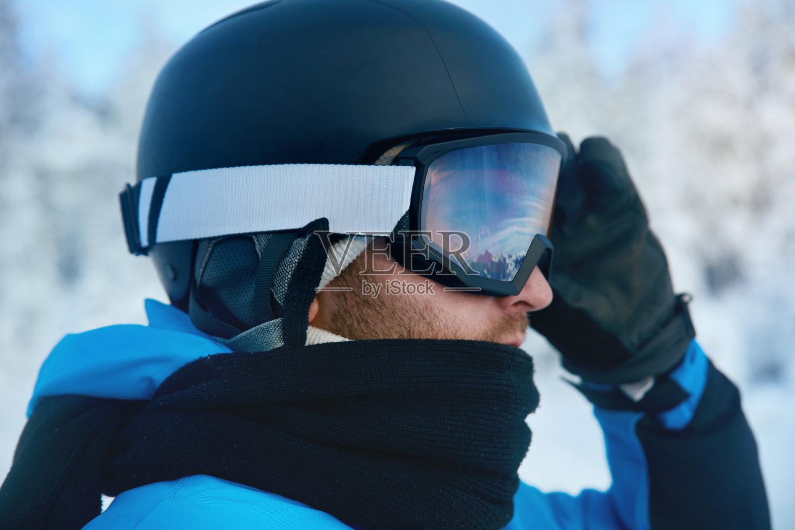男子滑雪镜的特写，镜片上反射着被雪覆盖的山脉。滑雪面罩上反射出一座山脉。背景是山脉和天空的男子肖像。照片摄影图片