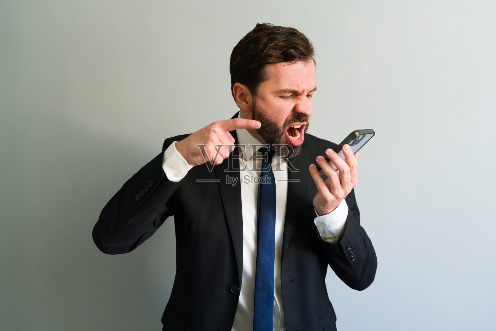 愤怒的商人在灰色背景下对着电话大喊照片摄影图片