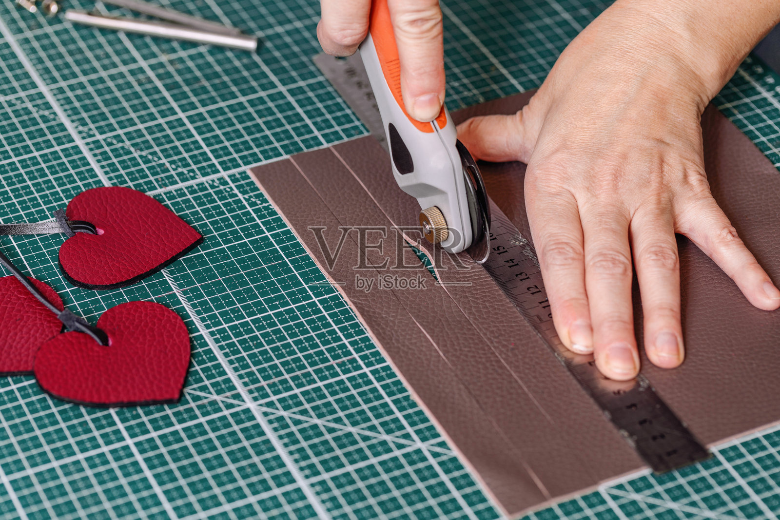 皮革工匠的手在绿色切割垫上使用工具切割皮革，特写，过程。照片摄影图片