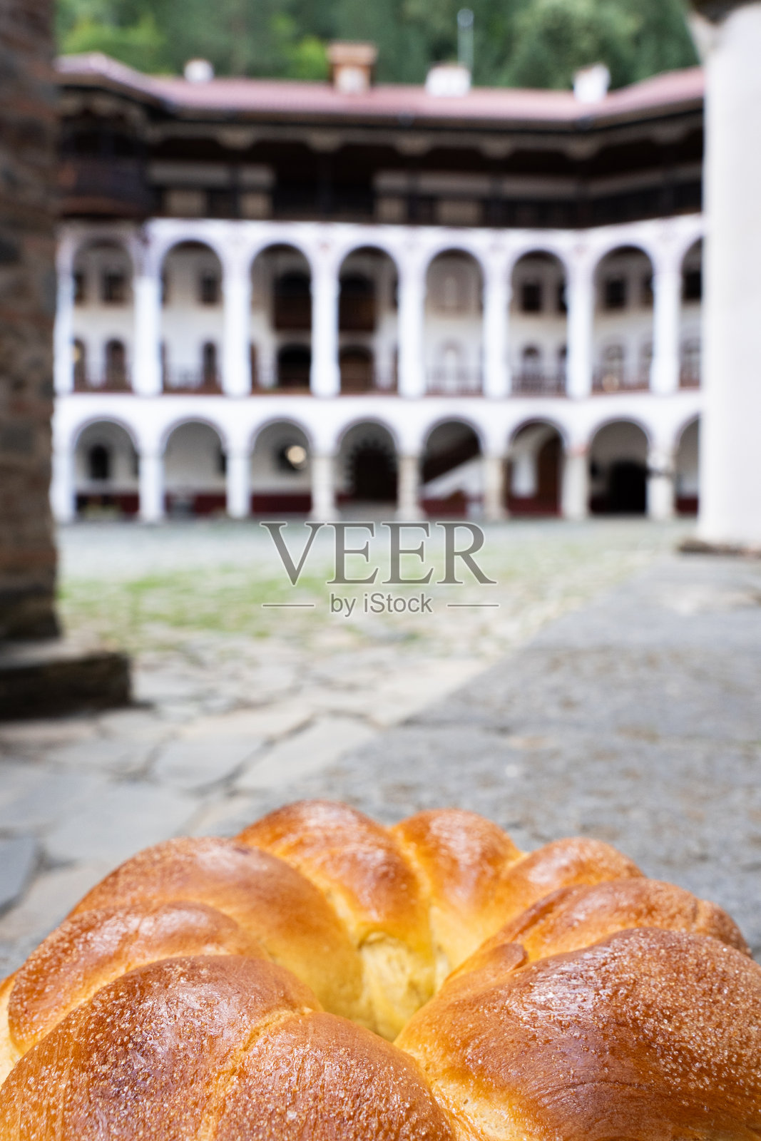 典型保加利亚金棕色面包的特写，背景是一个历史悠久的庭院，展示了传统建筑和烹饪遗产。画面中没有人。照片摄影图片