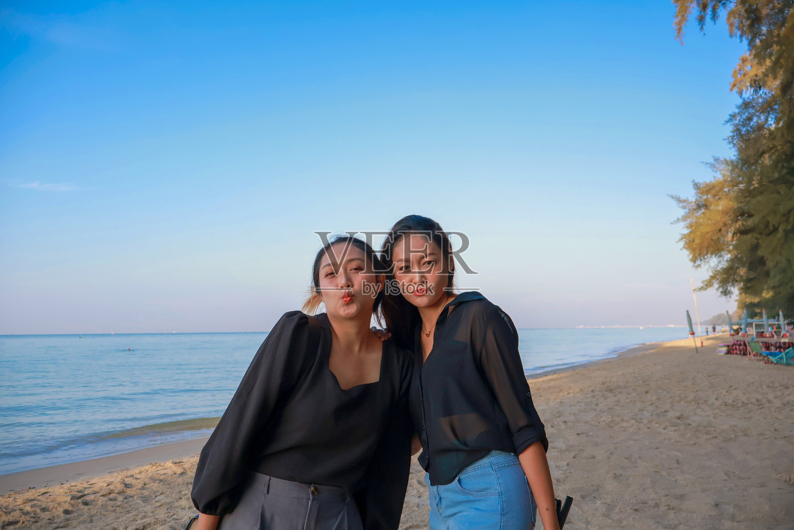快乐的亚洲女性姐妹在海滩上，蓝天背景下的旅行，地点为泰国罗勇省。照片摄影图片