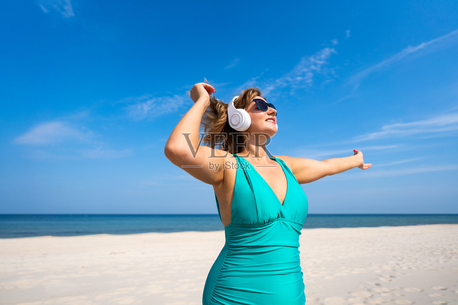 美丽的成熟的女性在白色沙滩上戴着耳机听音乐照片摄影图片