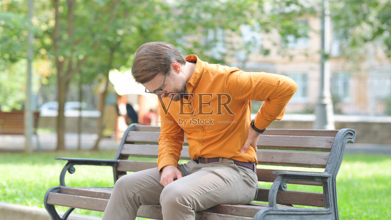 疲惫的年轻男子在户外坐着，感到背痛照片摄影图片