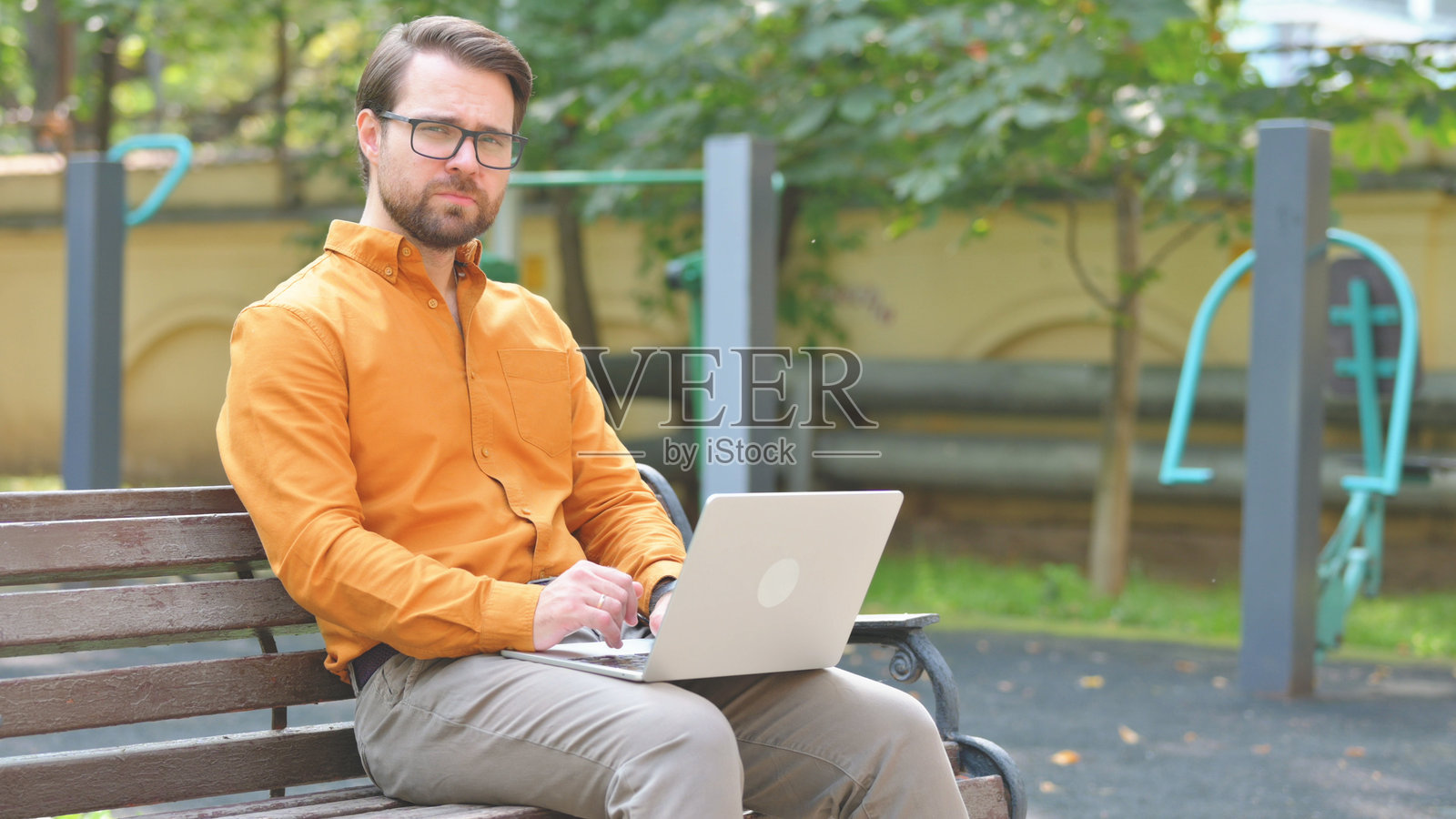 中年男子在户外坐着使用笔记本电脑并看向镜头照片摄影图片