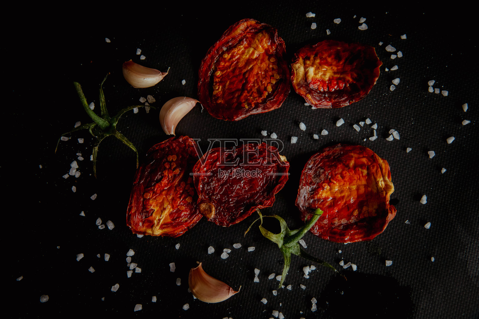 黑色背景上的晒干番茄片，配有香料和盐照片摄影图片