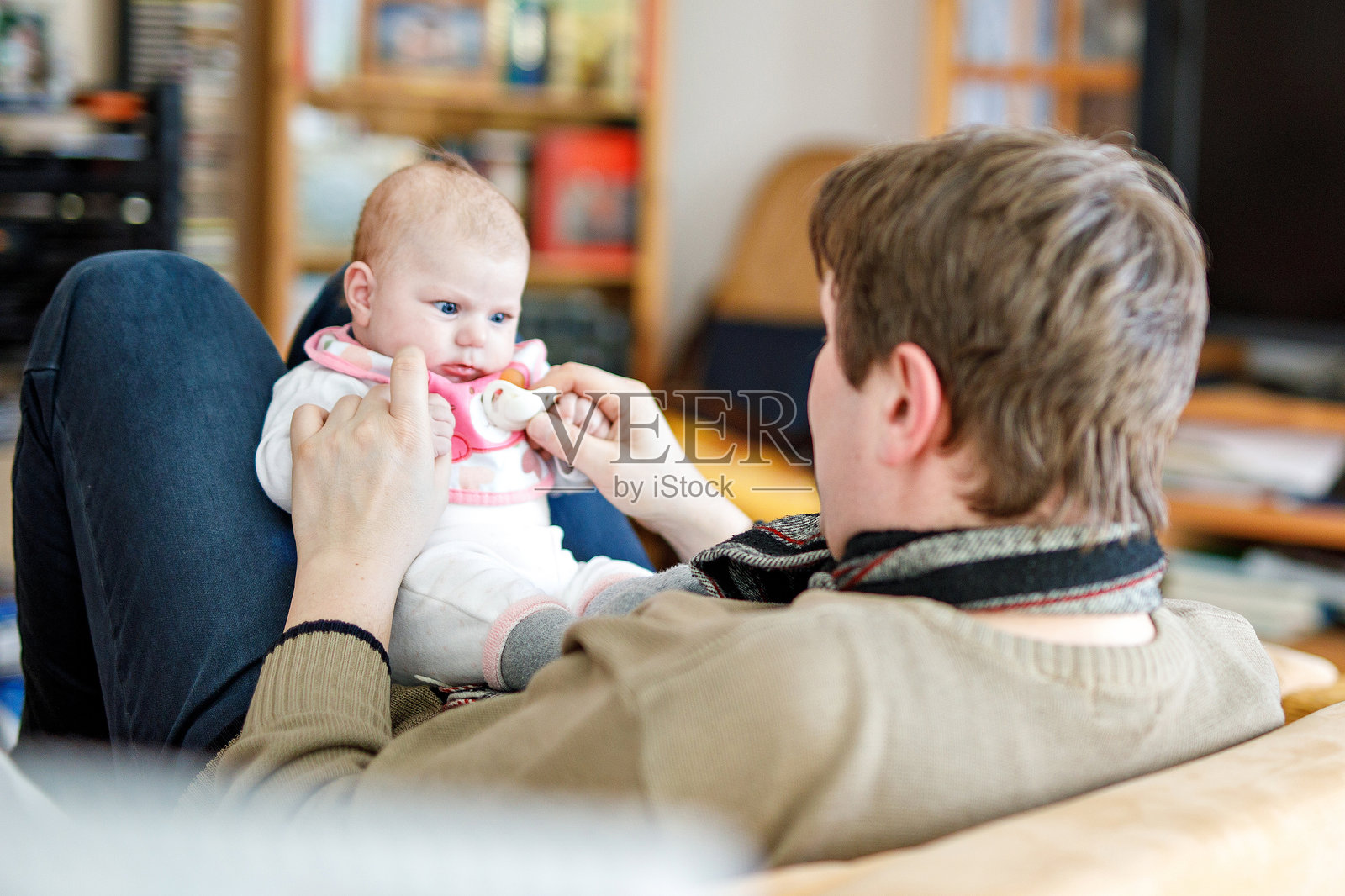 快乐自豪的年轻父亲与新生女儿一起享受乐趣，家庭合影。爸爸与小女孩，充满爱。新生儿注视着爸爸。亲密关系，家庭，新生活。照片摄影图片