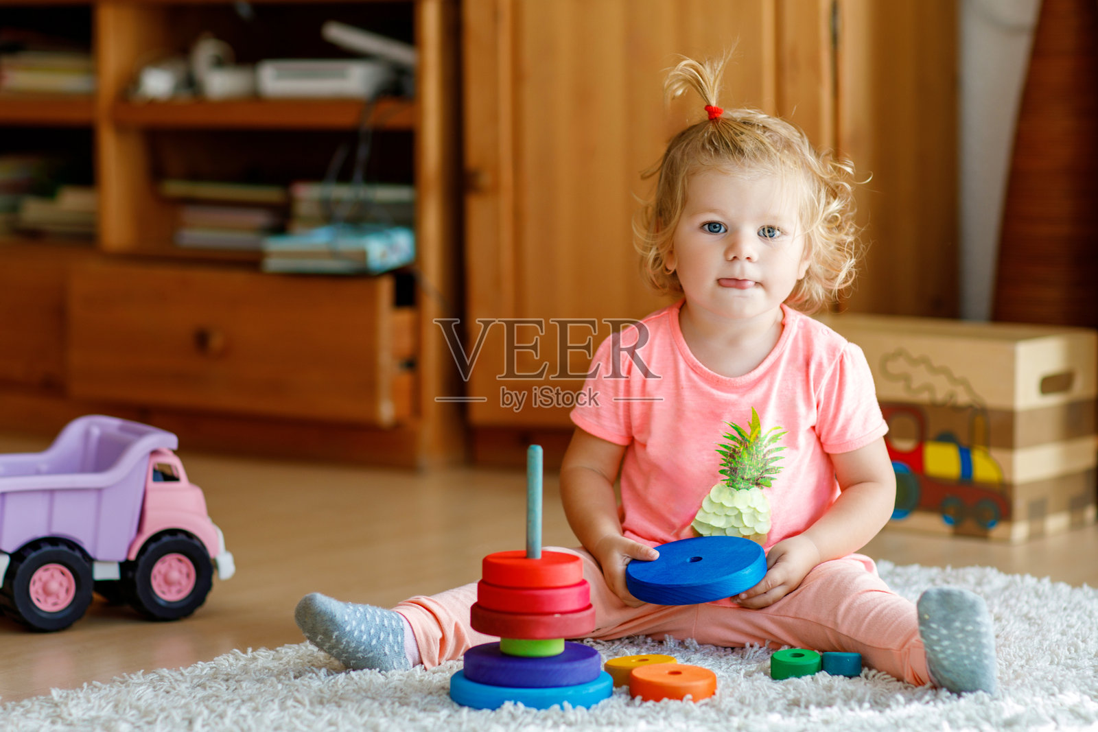 快乐的小女孩坐在地毯上，专注地玩着五颜六色的木环和玩具卡车，正在堆叠这些玩具。孩子在家里或幼儿园玩着彩虹色的金字塔。照片摄影图片