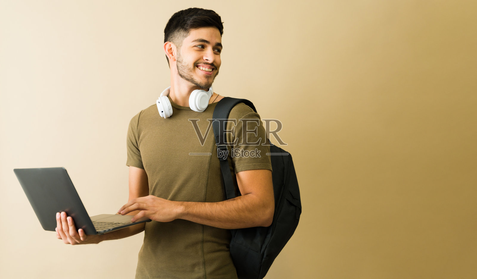 微笑的学生一边走一边使用笔记本电脑并向一旁看去照片摄影图片