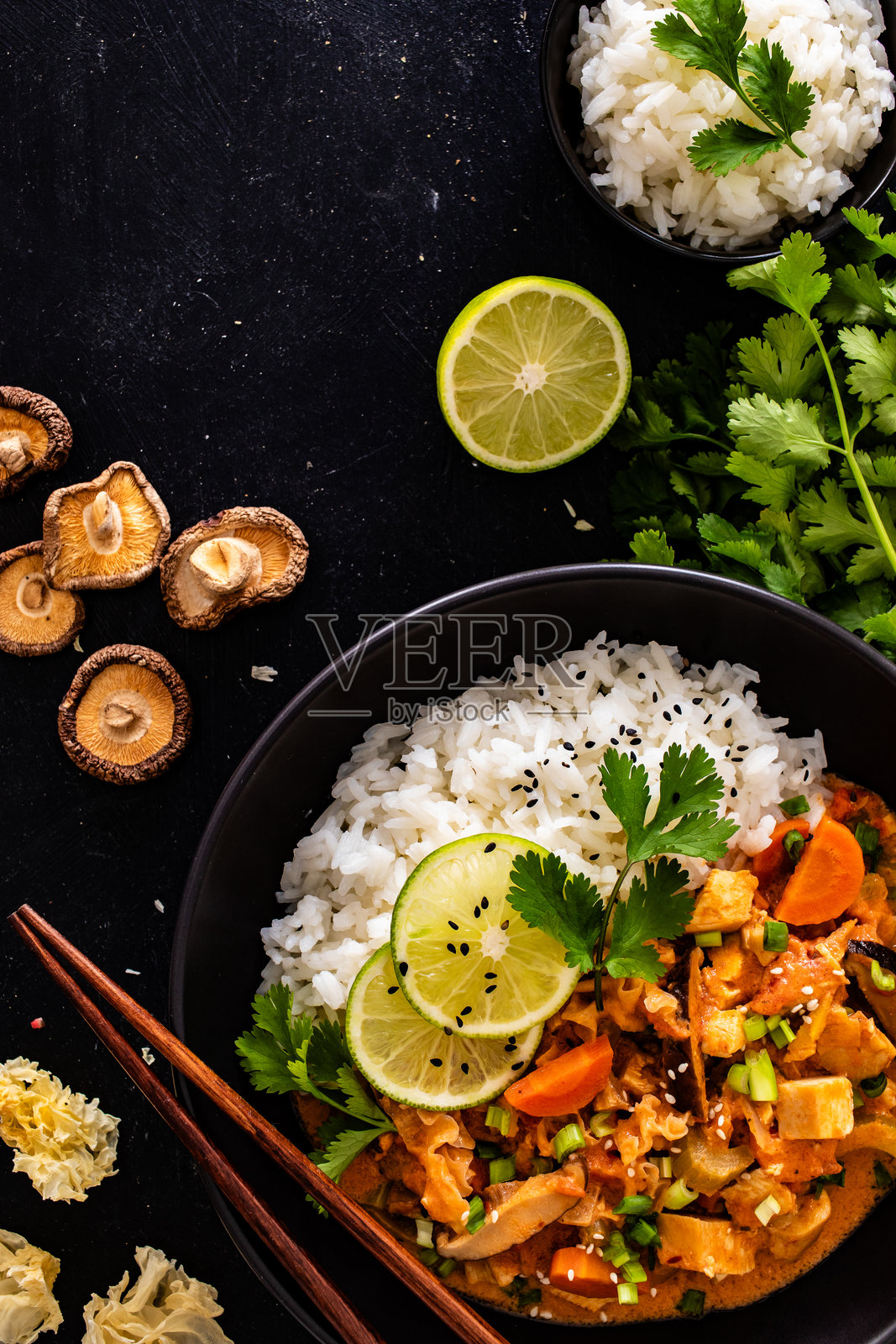 泰国菜 - 鸡肉块配蔬菜、蘑菇和米饭，浸泡在番茄和椰奶酱中，摆放在黑色桌子上照片摄影图片