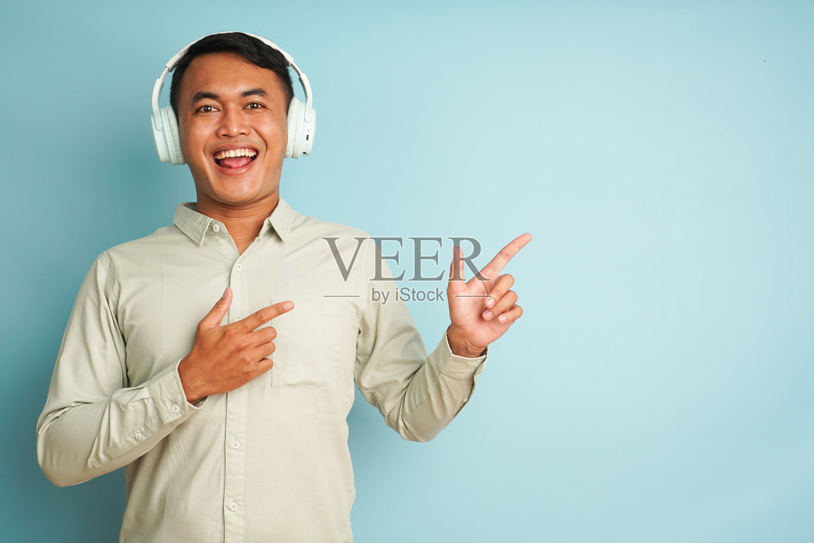 戴着耳机的男子指向蓝色背景的空白区域照片摄影图片