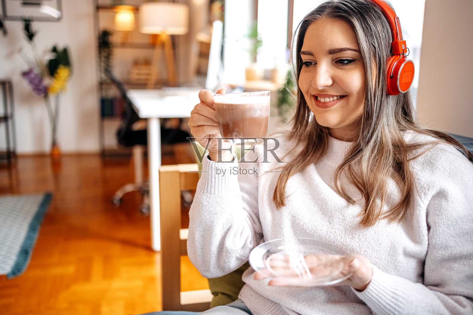 年轻漂亮的女人在家里独自享受咖啡，戴着无线耳机听音乐照片摄影图片