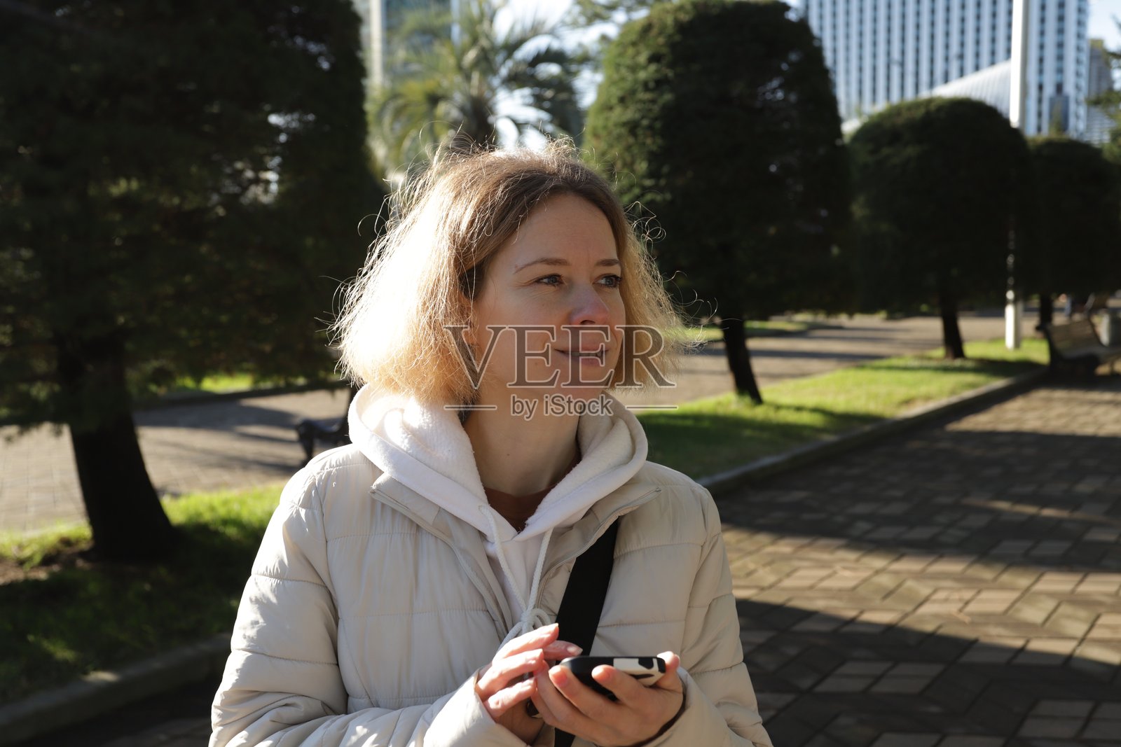 女性在城市户外使用智能手机，边走在大街上边查看智能设备上的信息，使用移动应用进行沟通和媒体交流。照片摄影图片