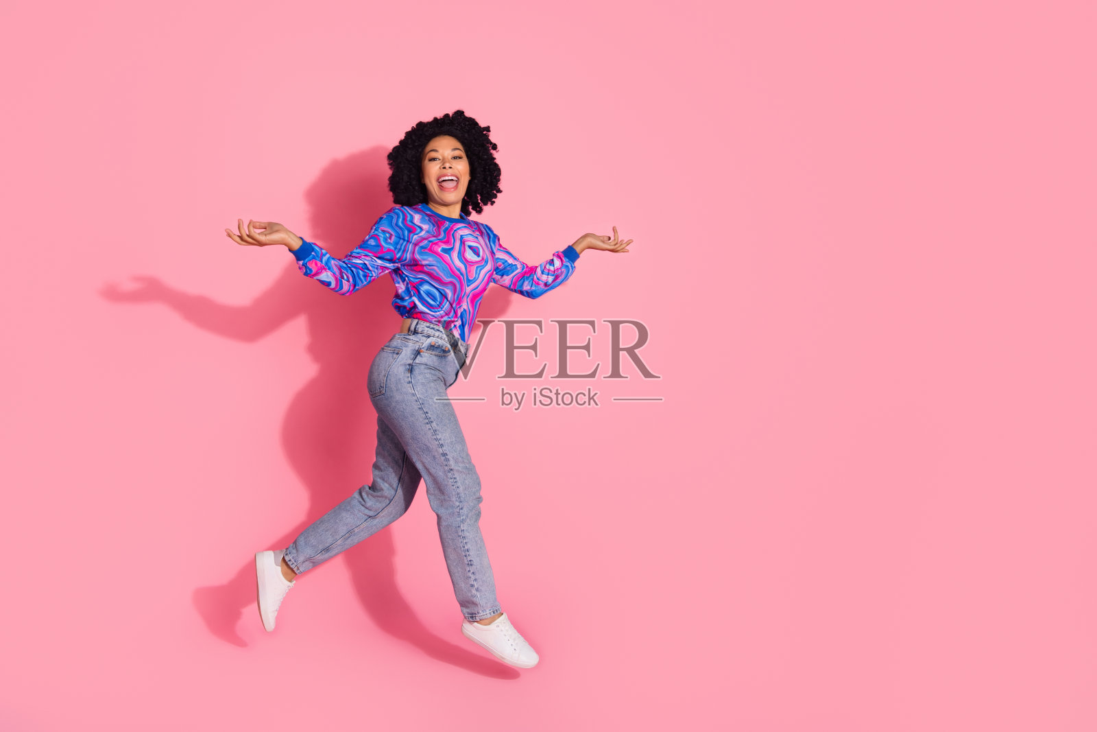 穿着时尚印花衣服的快乐积极女性在粉色背景上快速奔跑的照片照片摄影图片