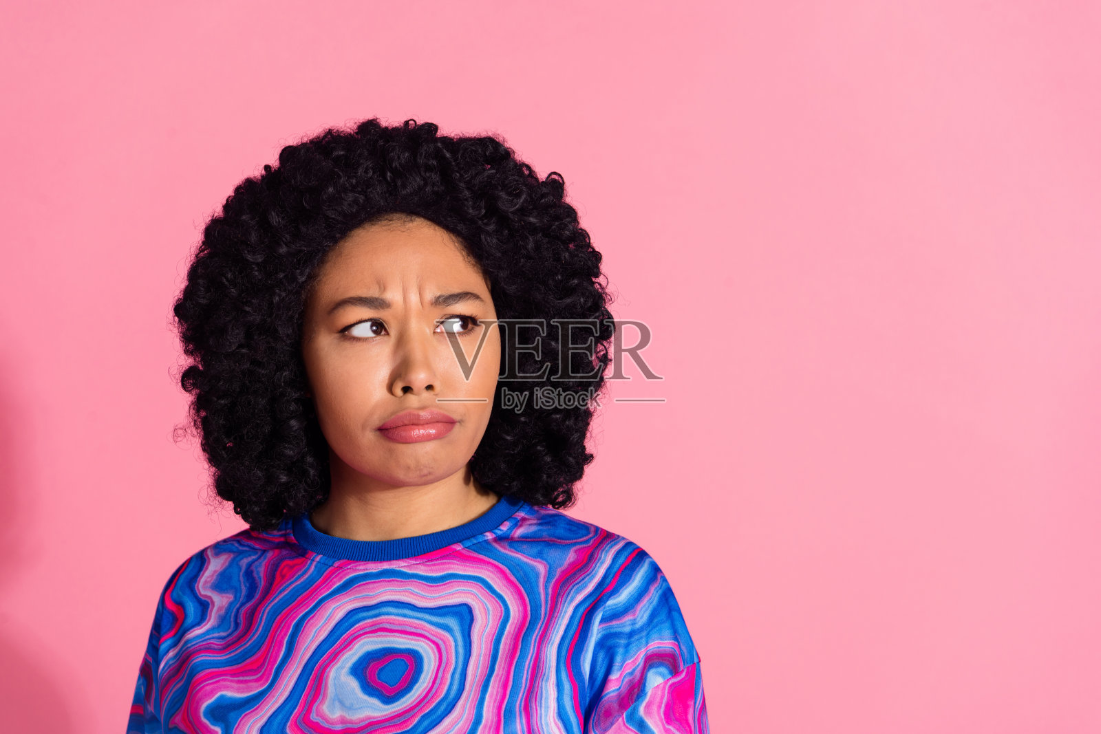 穿着时尚毛衣的可怜女孩，面带忧伤，望向空旷的空间，背景为粉色海报。照片摄影图片