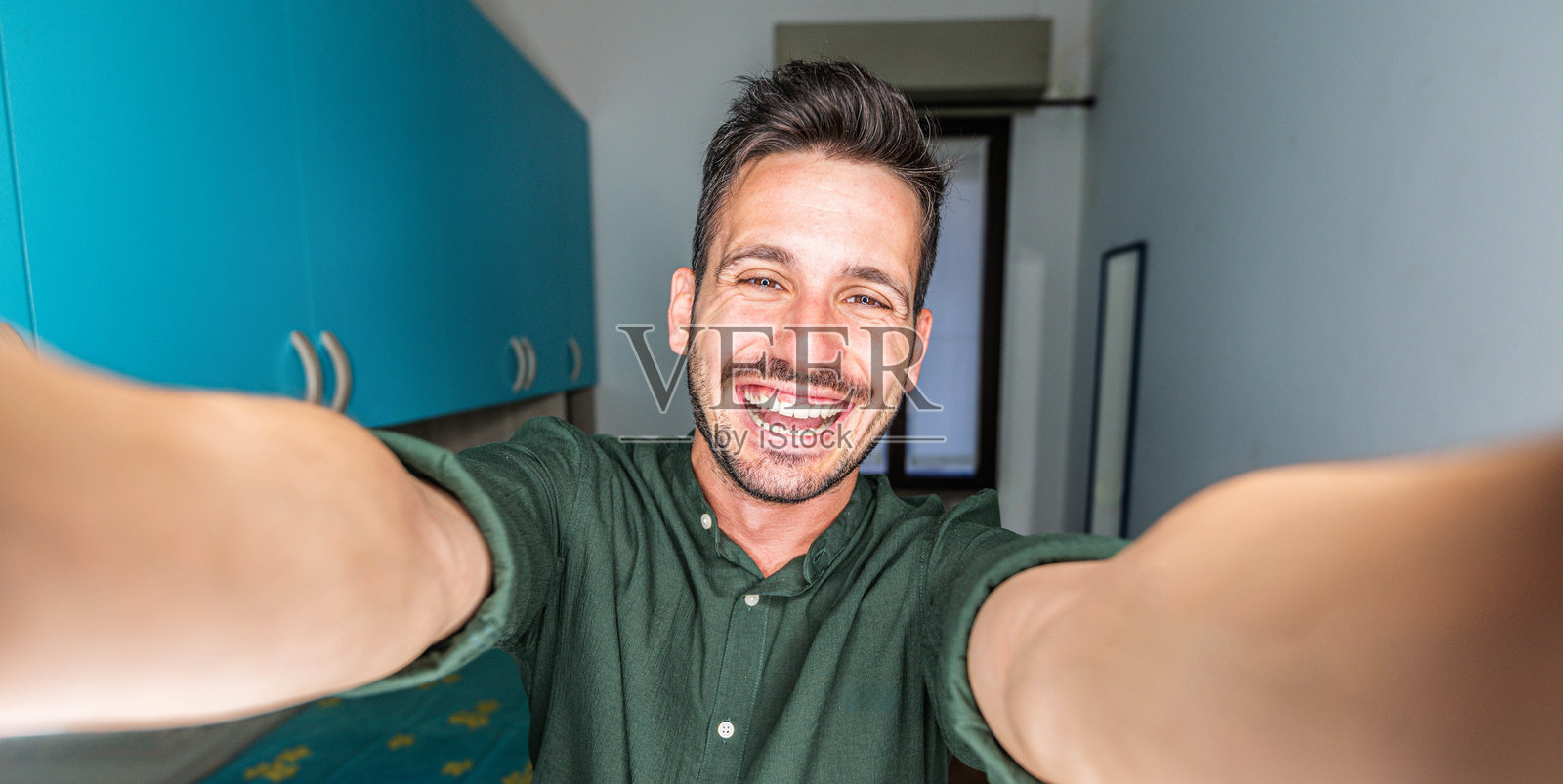 帅气的年轻男子在室内用智能手机自拍 - 微笑的男孩在家中看着镜头 - 人与科技的概念照片摄影图片