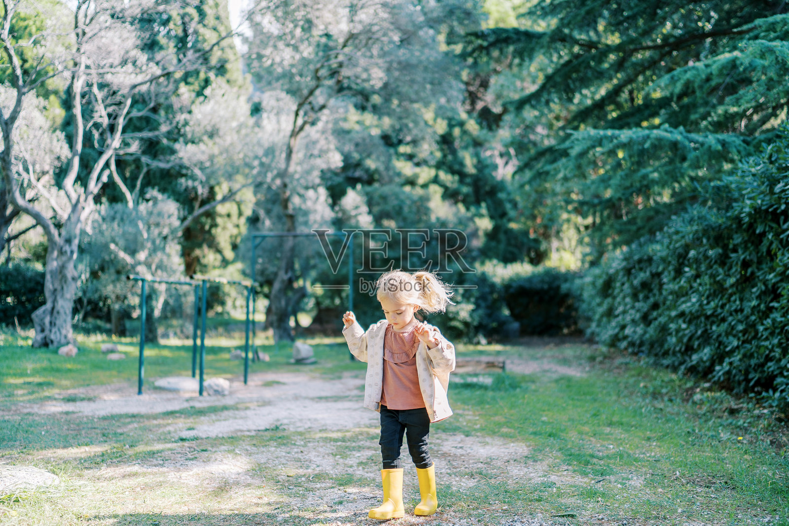 小女孩在绿色公园里走着，低头看着自己的脚。照片摄影图片