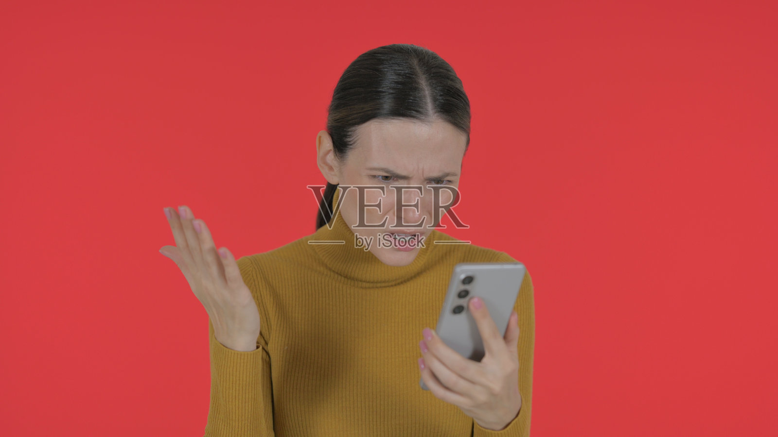 年轻女性因手机上的损失而感到震惊，红色背景，肖像画照片摄影图片
