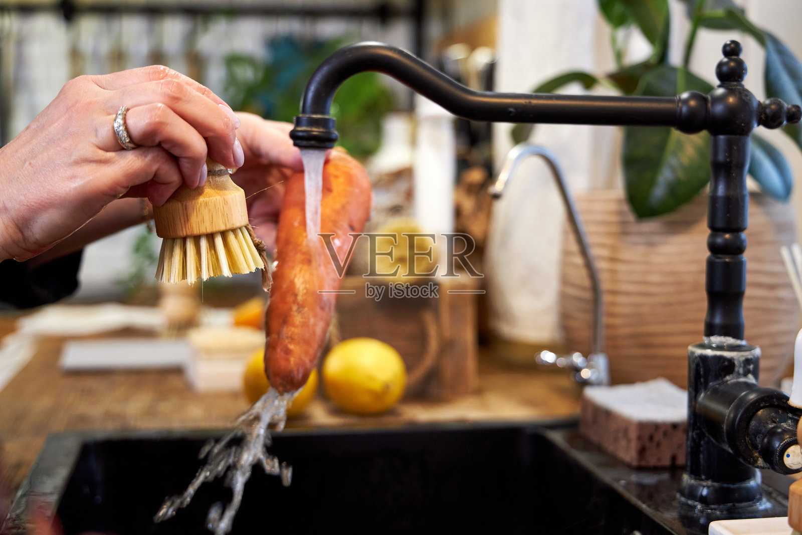 一位女性在现代黑色水槽中用木刷清洗蔬菜和胡萝卜。照片摄影图片