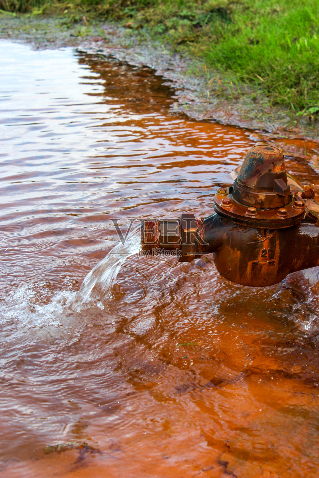一个生锈的旧水龙头，正在为一个人工湖注水照片摄影图片