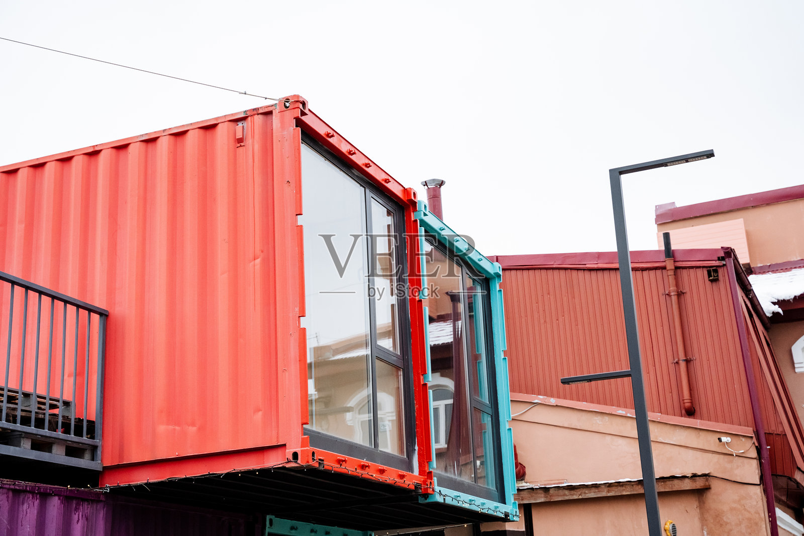一个鲜艳的红色集装箱，带有阳台，放置在一栋建筑旁边，形成了颜色和材料的有趣对比，同时提升了城市景观。照片摄影图片