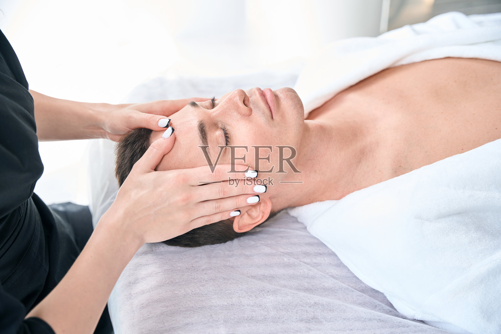 年轻男性在水疗中心享受抗衰老的面部放松按摩照片摄影图片