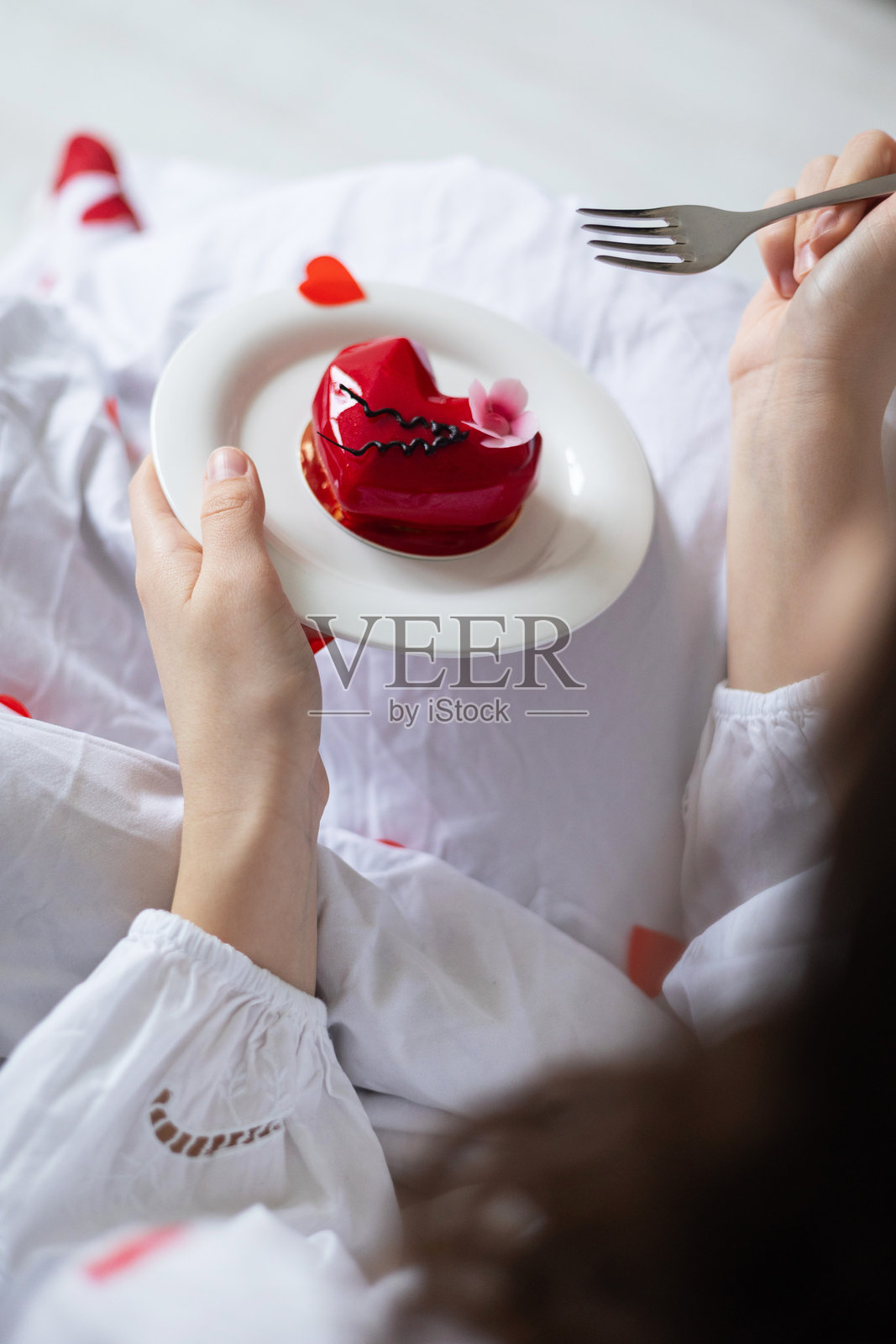 女性手部特写，手握白色盘子，上面放着蛋糕，床上。照片摄影图片