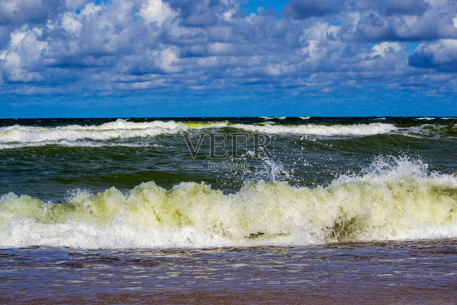 海浪在多云的天空下拍打着沙滩，展现出鲜艳的蓝色调照片摄影图片