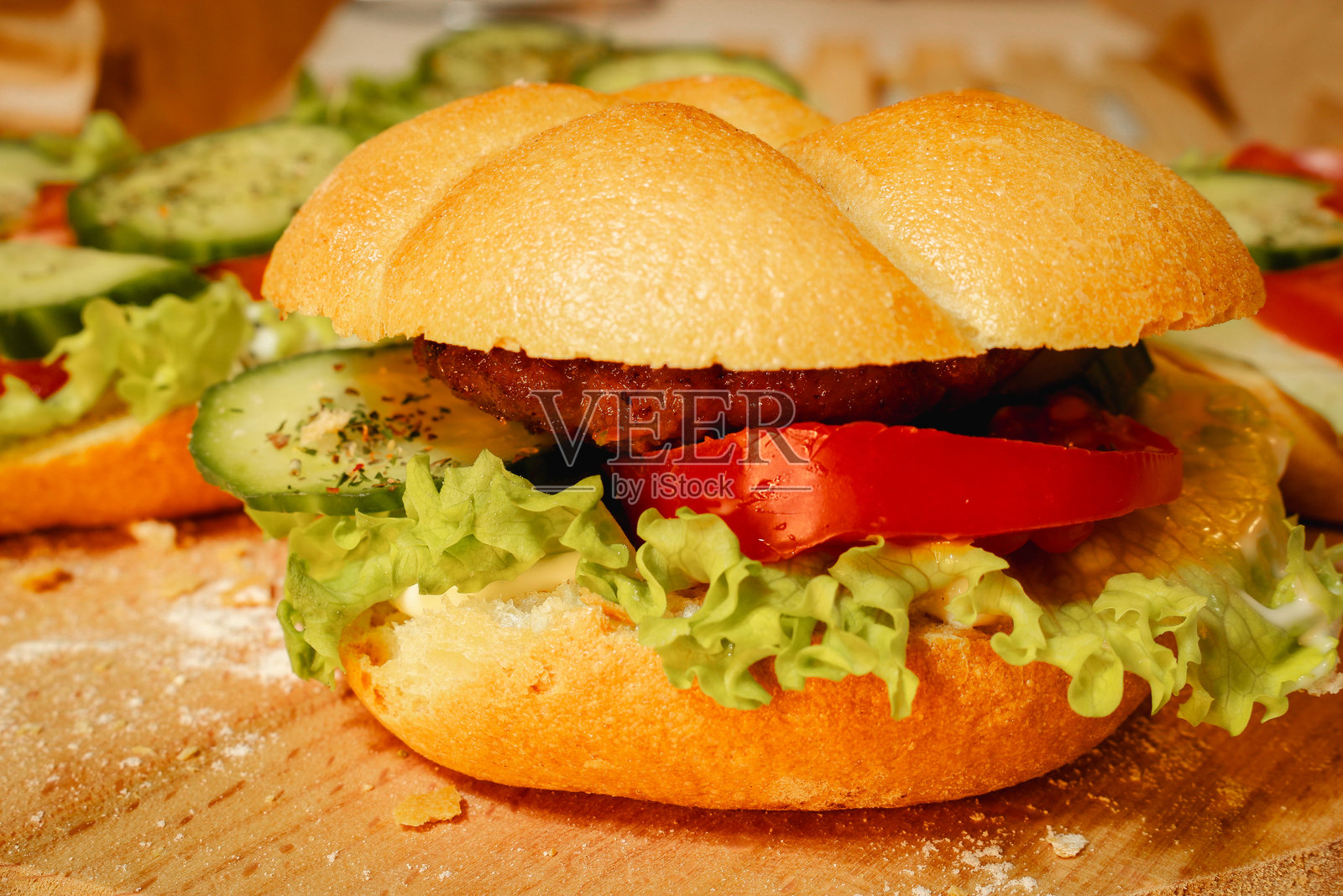 美味汉堡的照片，配有肉、番茄、黄瓜、新鲜生菜和柔软的面包，摆放在木板上。照片摄影图片