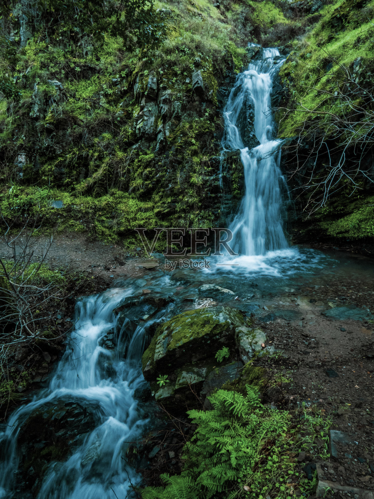 瀑布从苔藓覆盖的山丘倾泻而下照片摄影图片