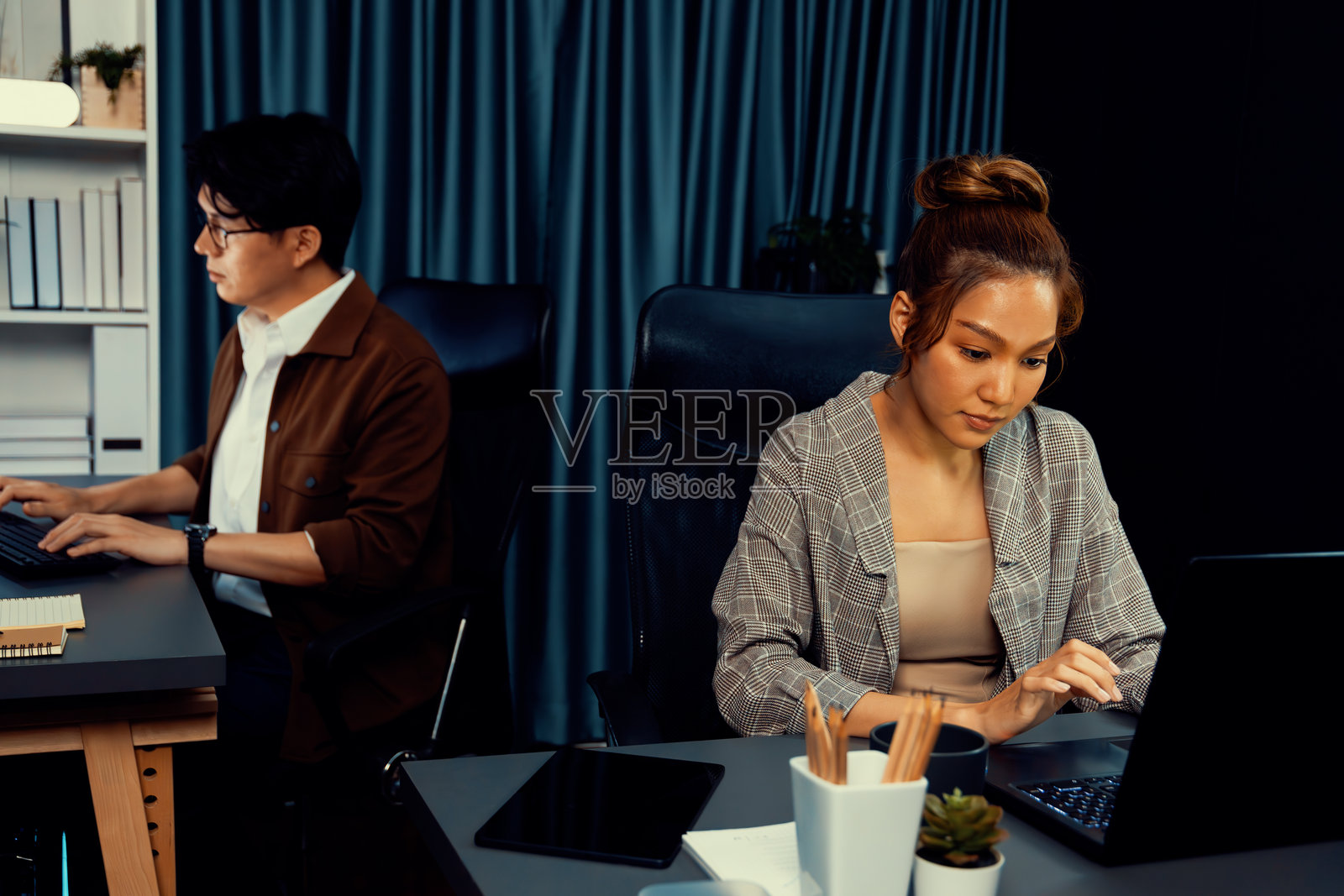 专注于电脑的女商人与在后面工作的同事。信息高速公路。照片摄影图片