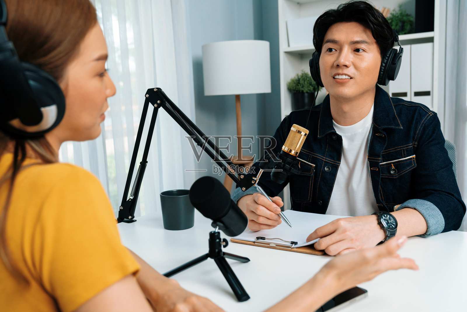 戴着耳机的广播影响者主持人与女性进行社交在线采访。信息高速公路。照片摄影图片