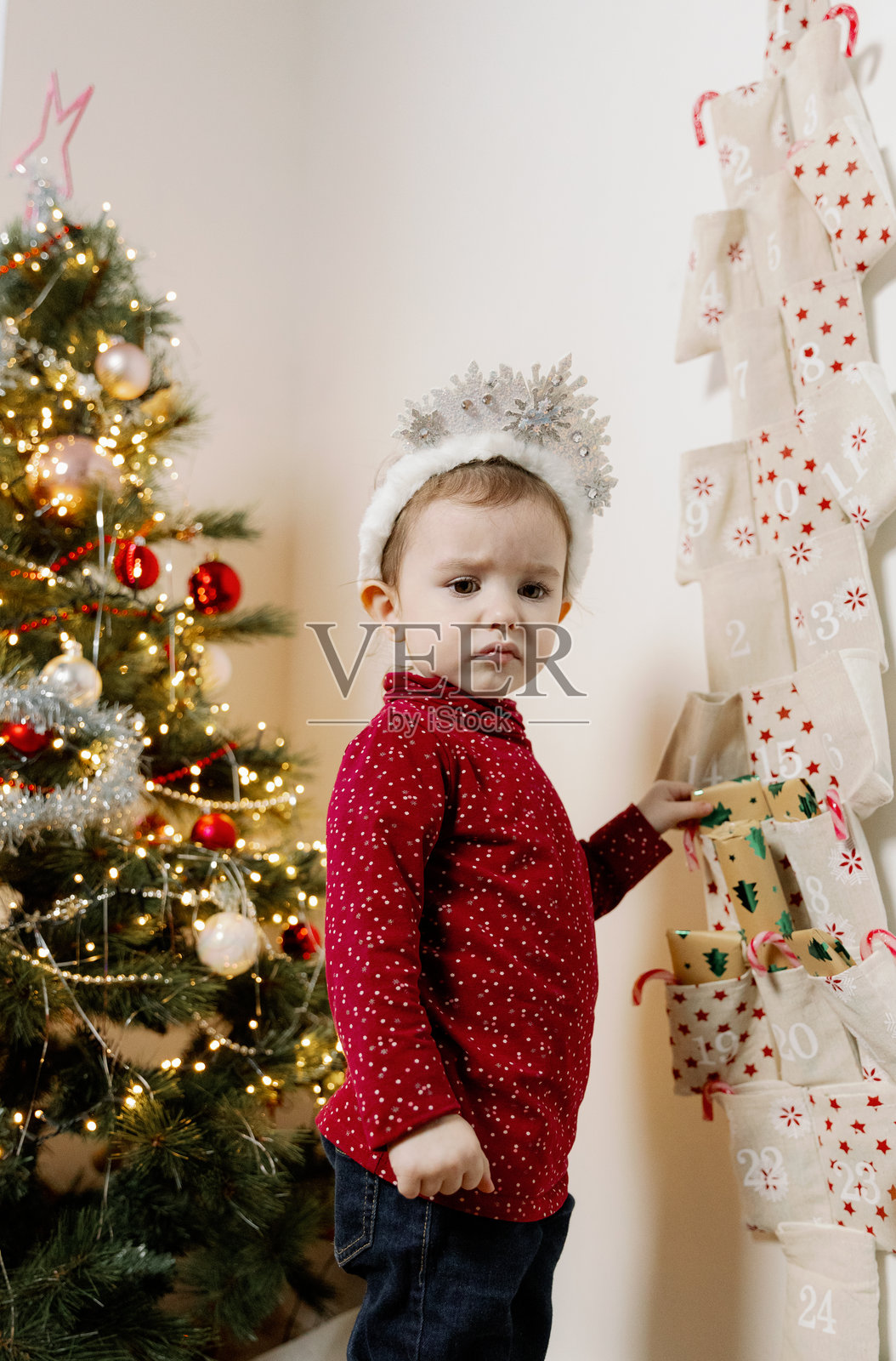 一个小女孩在圣诞树旁从降临日历中拿出一个礼物。照片摄影图片