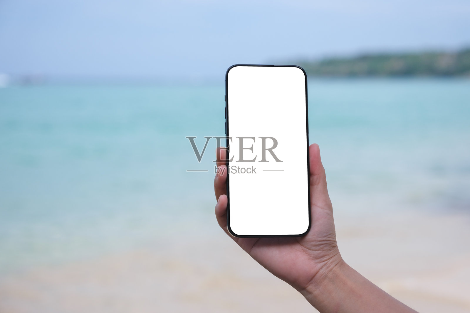 一位女性在海边手持手机，旁边是空白的桌面屏幕的模型图像照片摄影图片