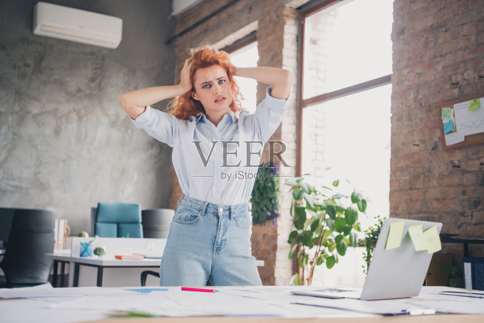 年轻女职员在现代阁楼风格的商务中心室内，双手触碰头部，显得有些困惑。照片摄影图片