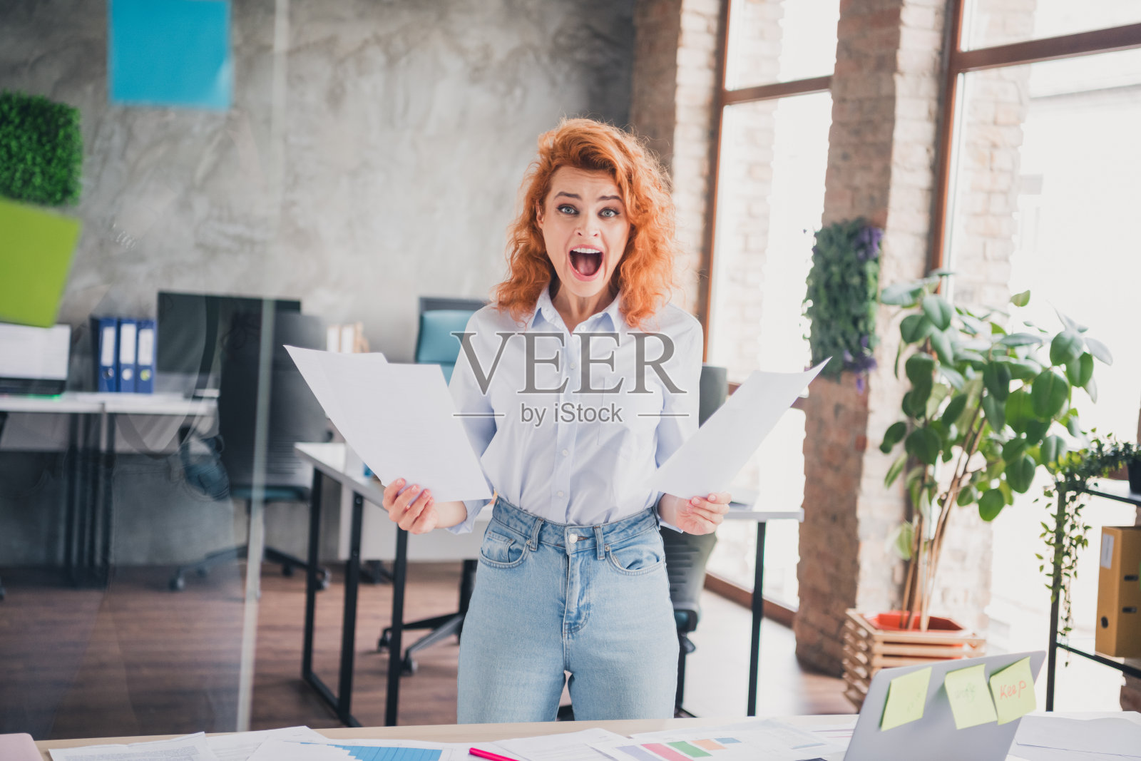 年轻女职员在现代阁楼风格的商务中心室内手持文件大声喊叫的肖像照片摄影图片