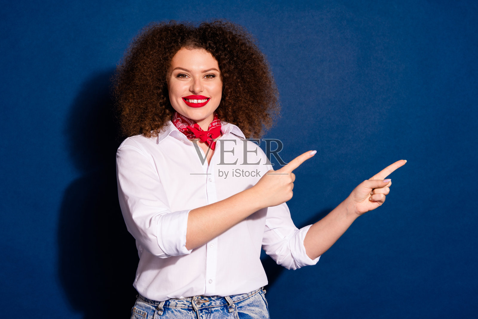 穿着红色手帕的迷人女士在蓝色背景下展示两个手指，空旷的空间。照片摄影图片