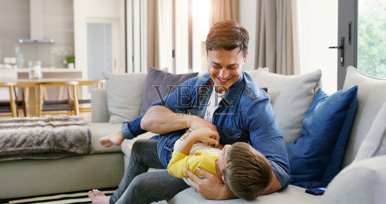 父亲与孩子在沙发上玩耍，增进亲情、联系或幸福的家庭关系。家庭中，男人与男孩一起在沙发上玩乐，享受关爱、快乐或安全感。照片摄影图片