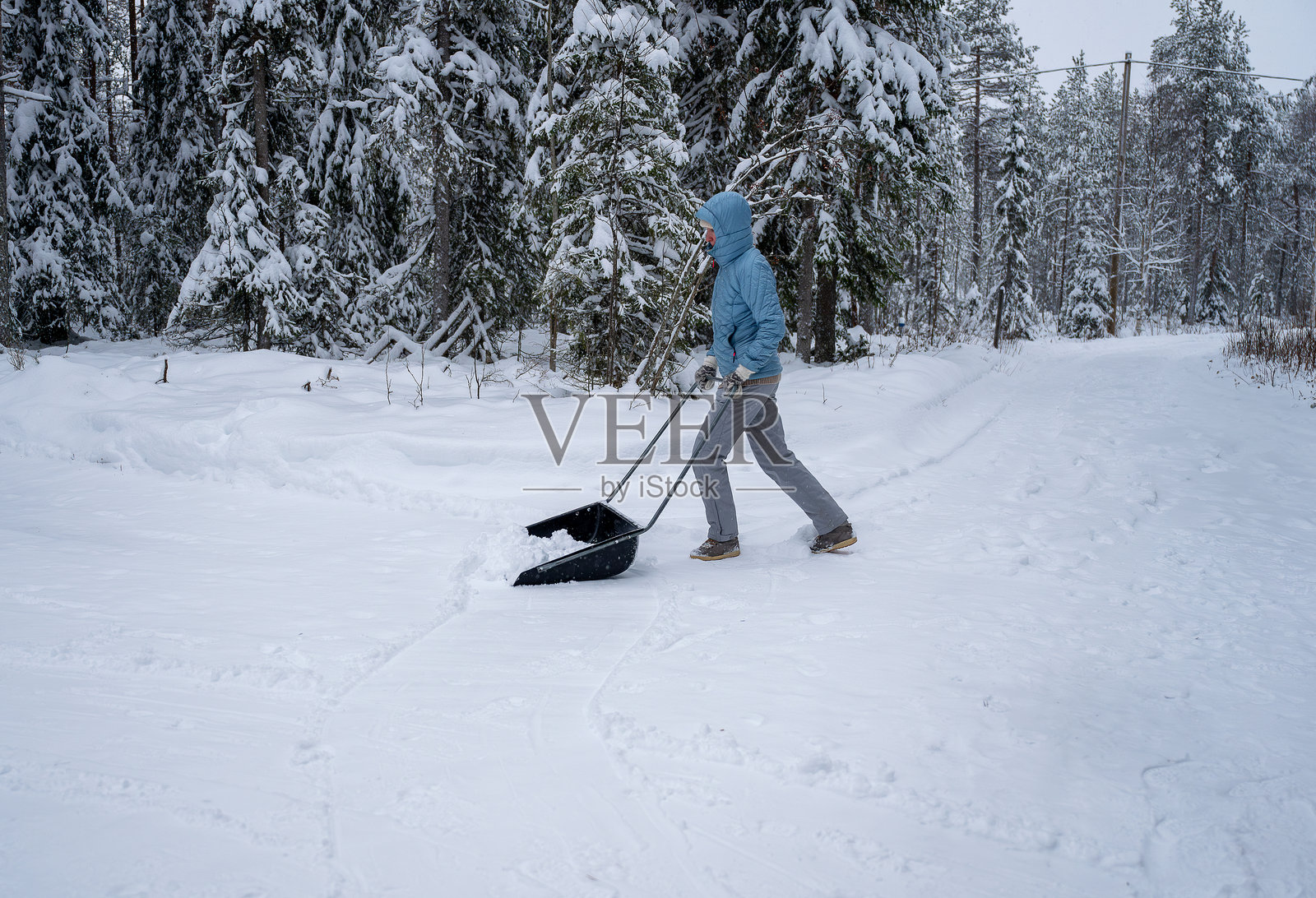 穿着冬季服装的女性在户外用刮雪器清理积雪照片摄影图片