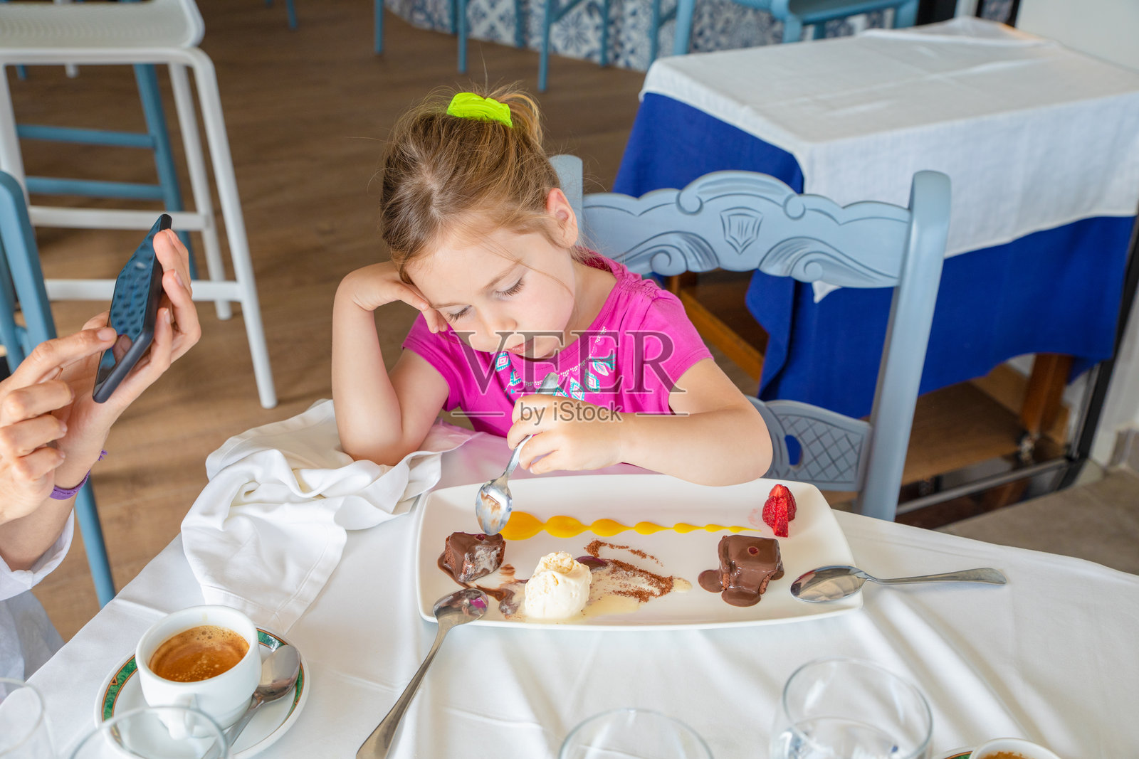 小女孩在餐厅里吃甜点，母亲则在用手机。照片摄影图片