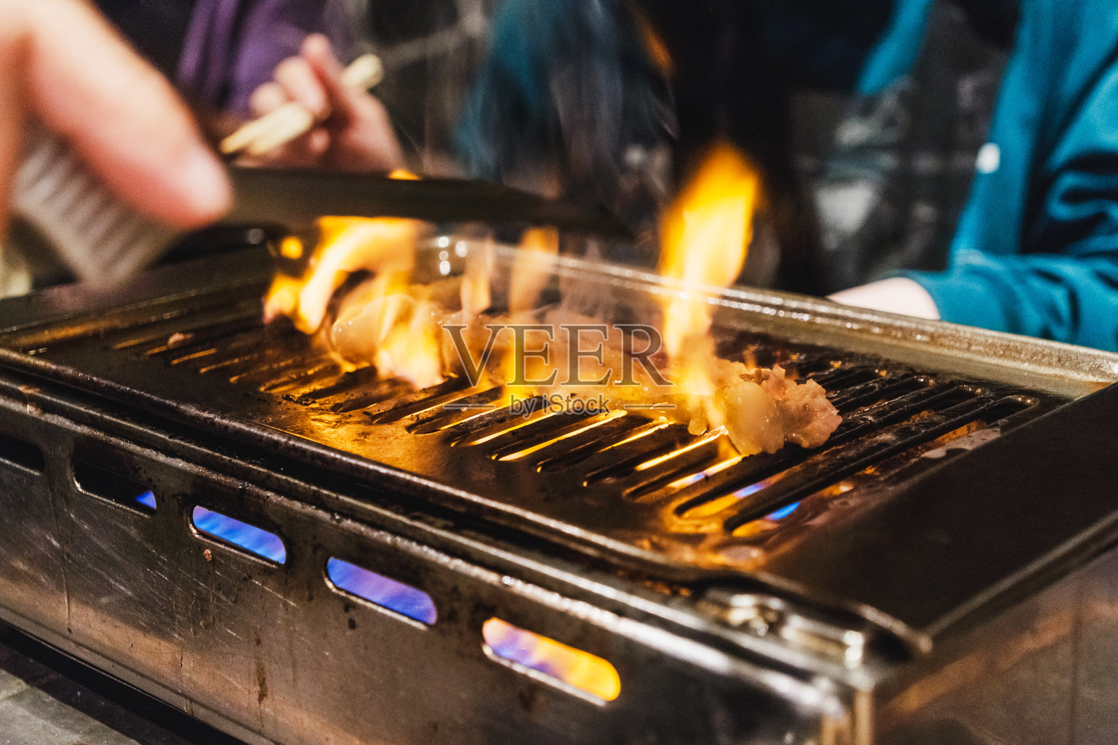 在日本烧肉餐厅的桌面烧烤上，肉类在明火上烤制。火焰腾起，食客们自己烹饪食物，营造出热闹的用餐体验。拍摄于日本东京。照片摄影图片