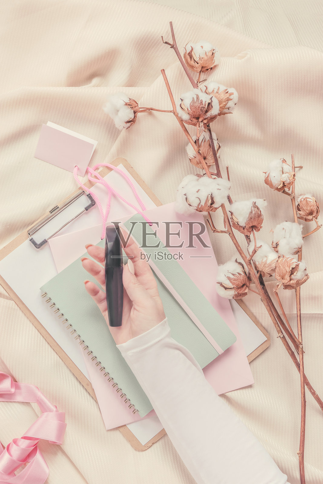 妇女们手里拿着化妆品，上面有米色的褶皱织物，上面有棉质的树枝和笔记本。照片摄影图片