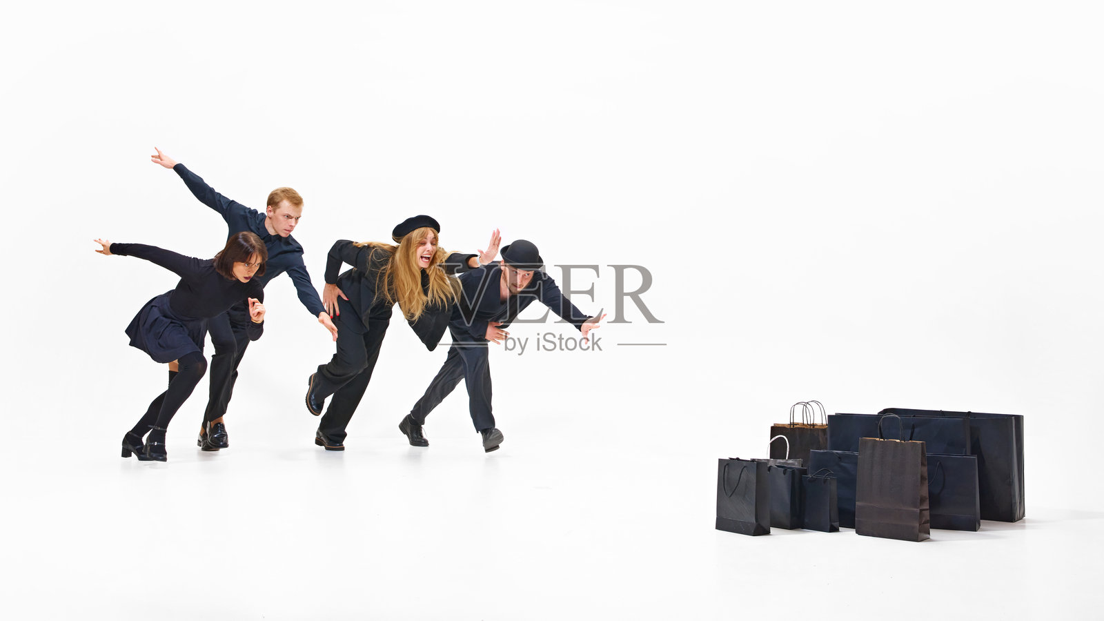 一群身穿黑色服装的人准备奔跑，朝着一堆诱人的黑色购物袋冲去，准备抢夺他们的战利品。照片摄影图片