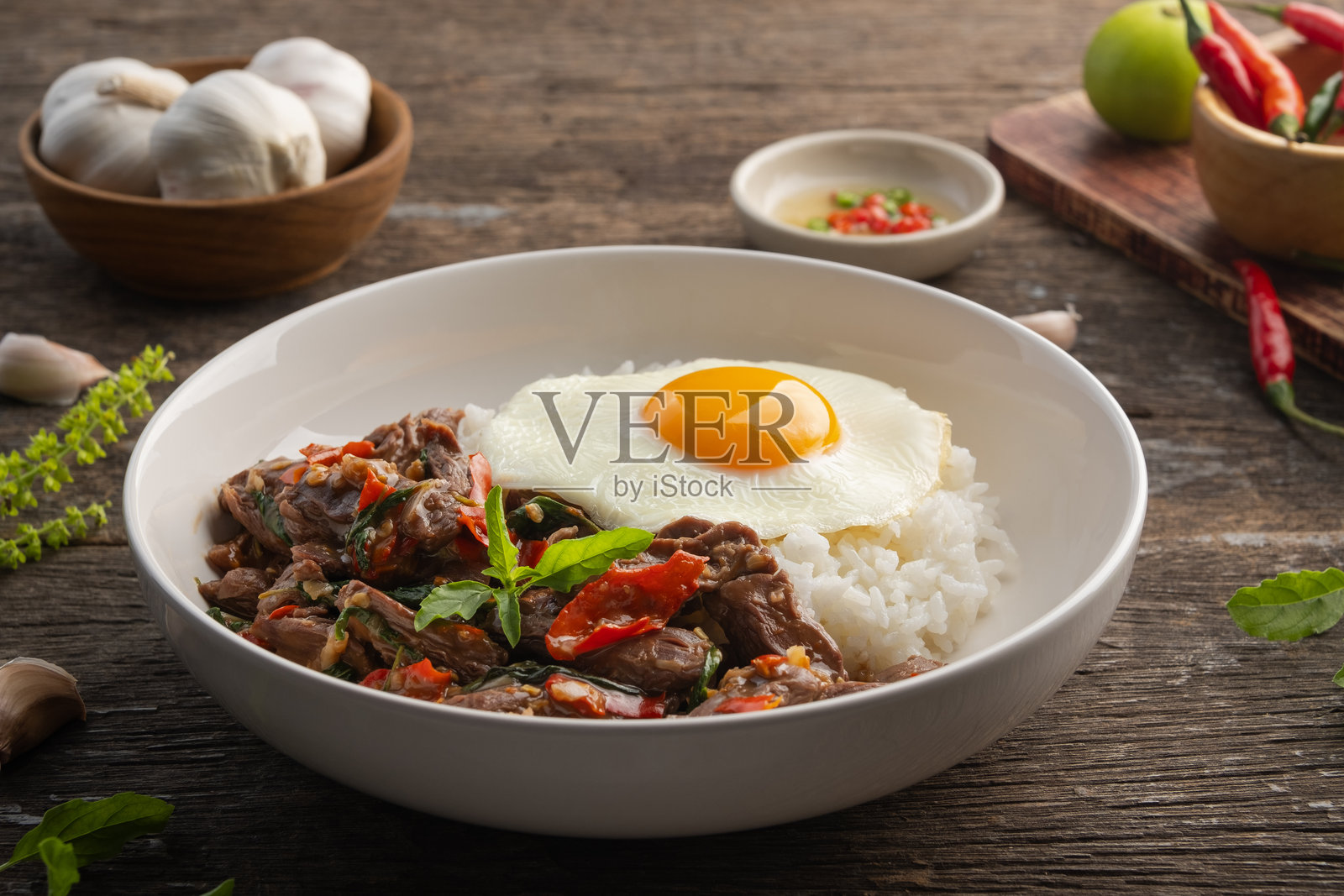 炒牛肉片配圣罗勒和米饭，上面放着煎蛋，盛在黑色盘子里。照片摄影图片